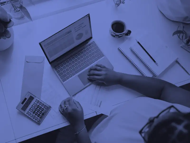 Vista de cima de uma mesa com notebook aberto numa planilha, calculadora e documentos